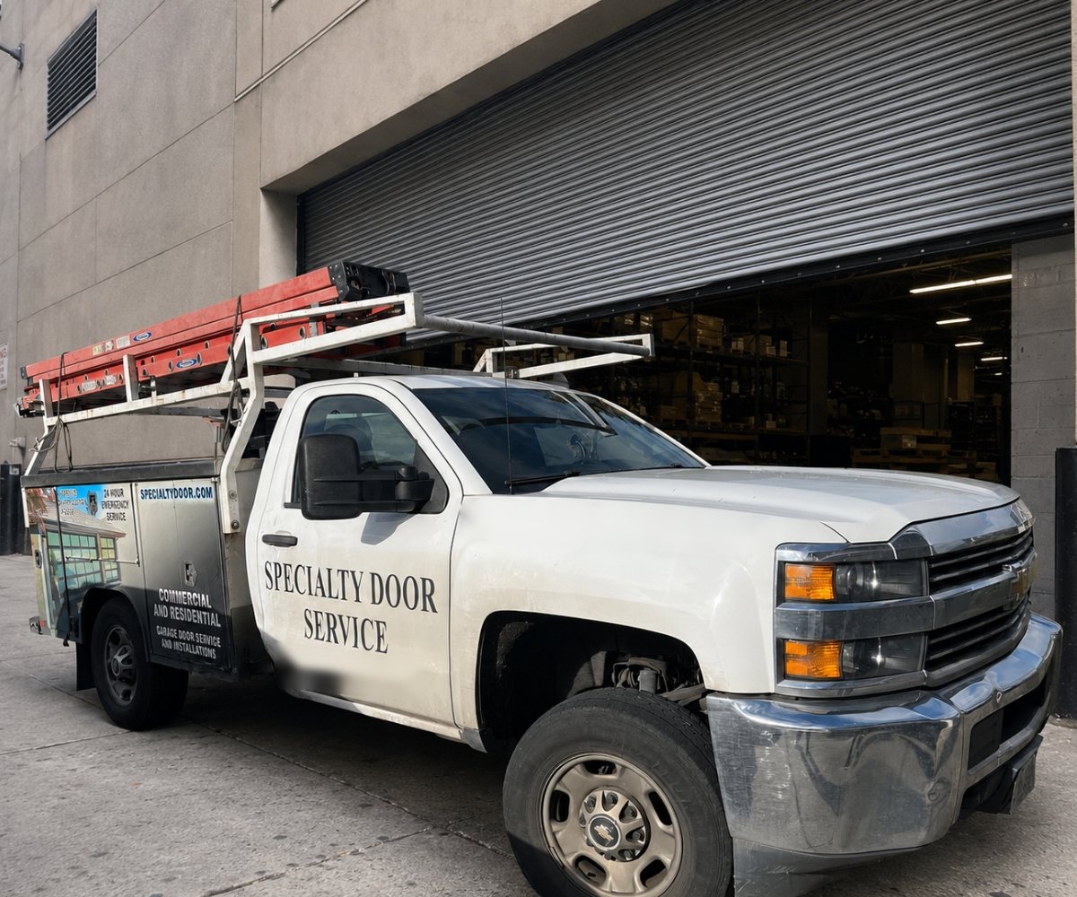 Specialty Door Service truck with ladders parked at a large rolling steel door