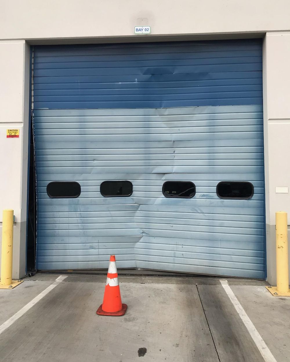 Loading dock door crushed at the bottom, with a traffic cone in front