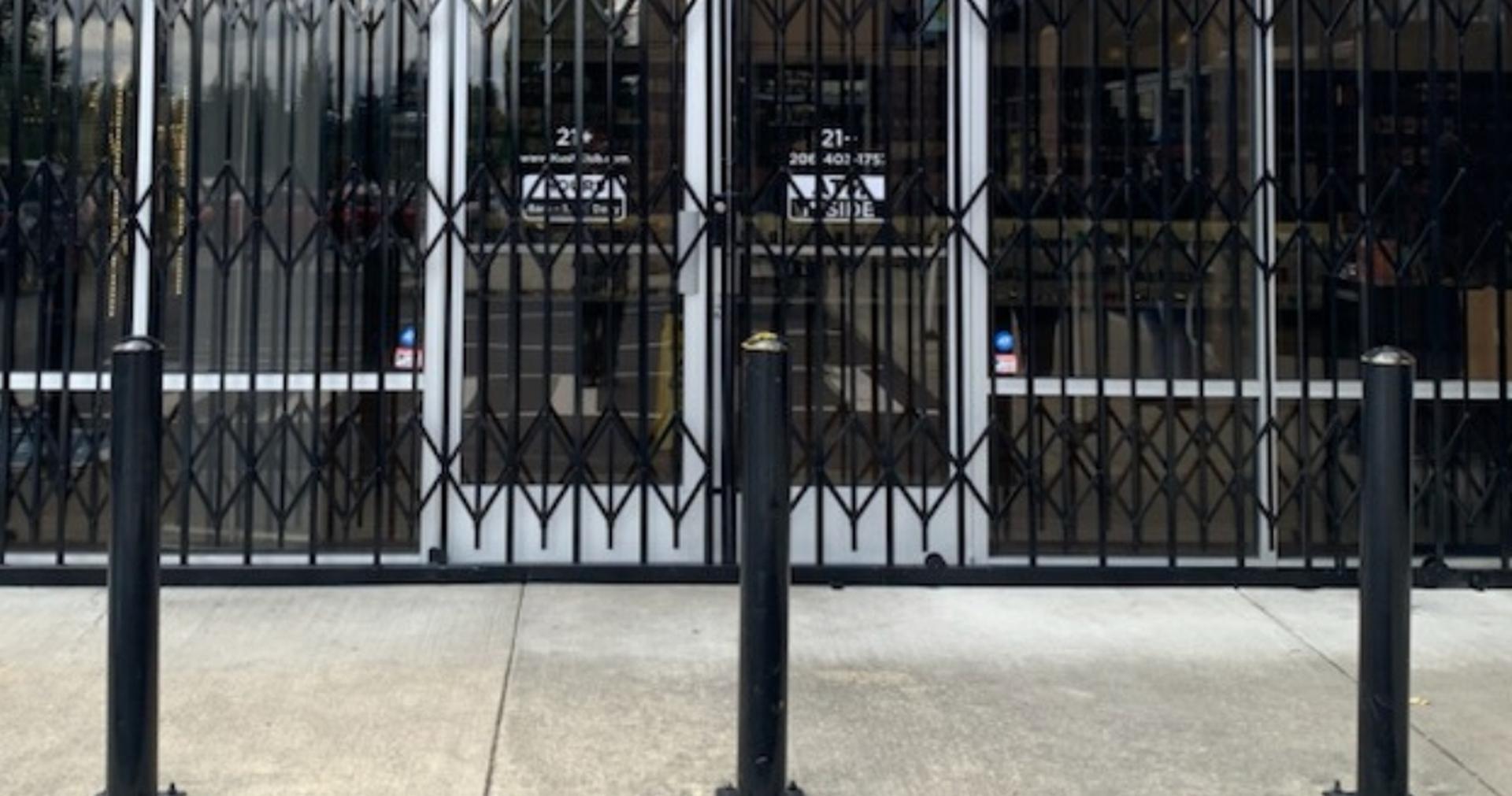 Folding security gates closed across a storefront, with bollards in front